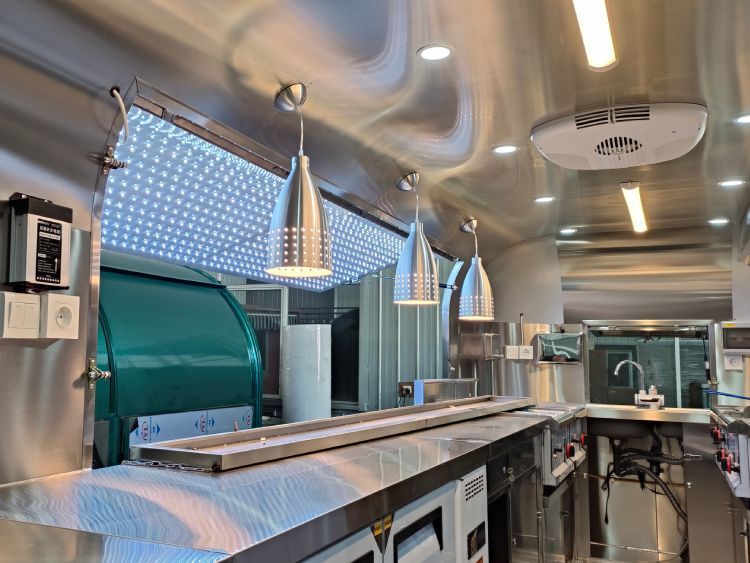 Intérieur moderne en inox d'un camion traiteur avec comptoirs et lampes.