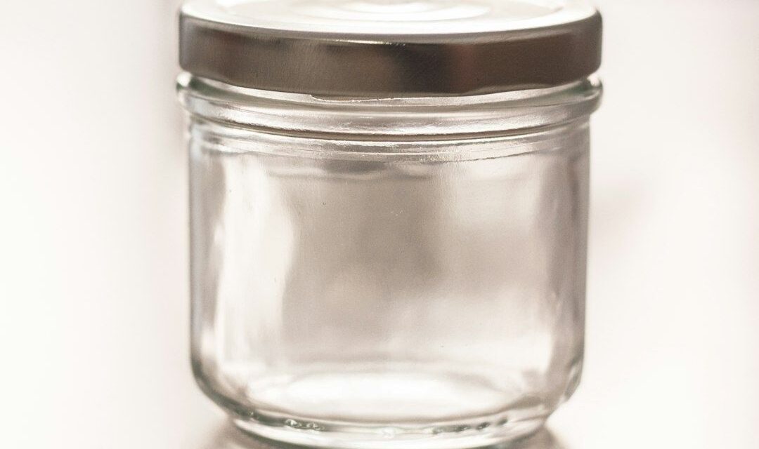 Petit bocal en verre vide avec couvercle métallique, posé sur une surface claire