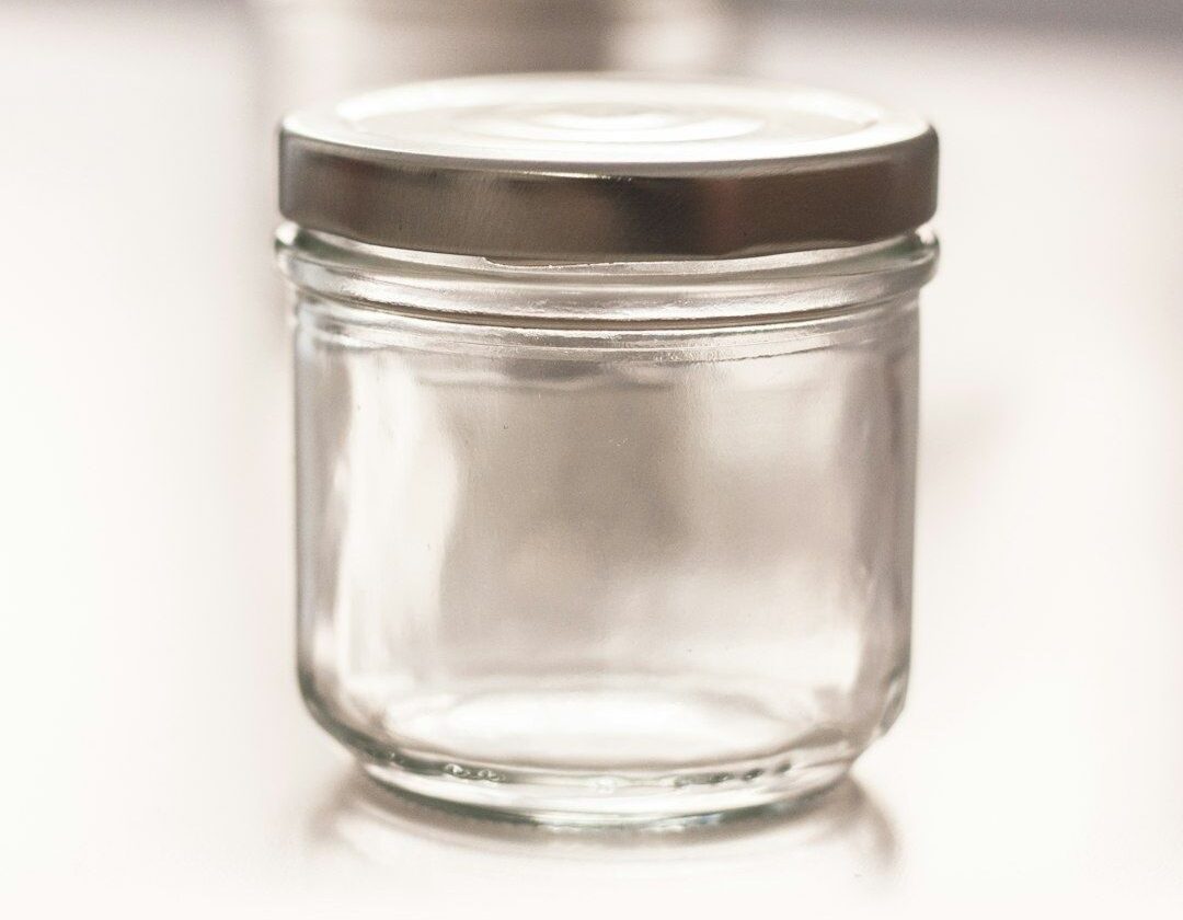 Petit bocal en verre vide avec couvercle métallique, posé sur une surface claire