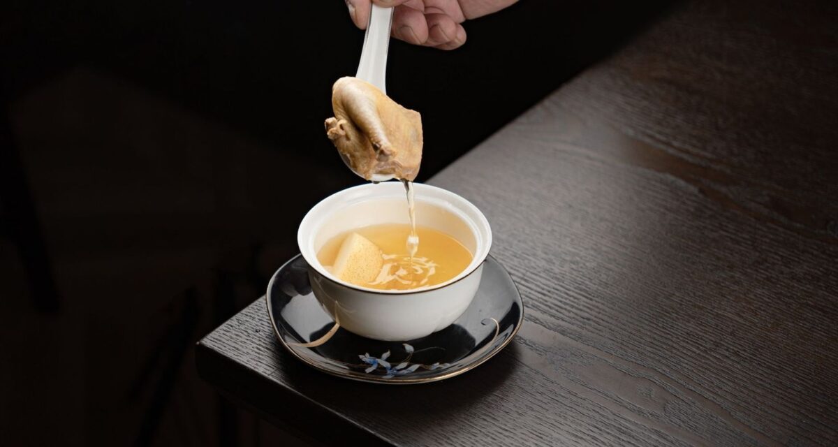 Une cuillère verse un bouillon doré dans une tasse blanche