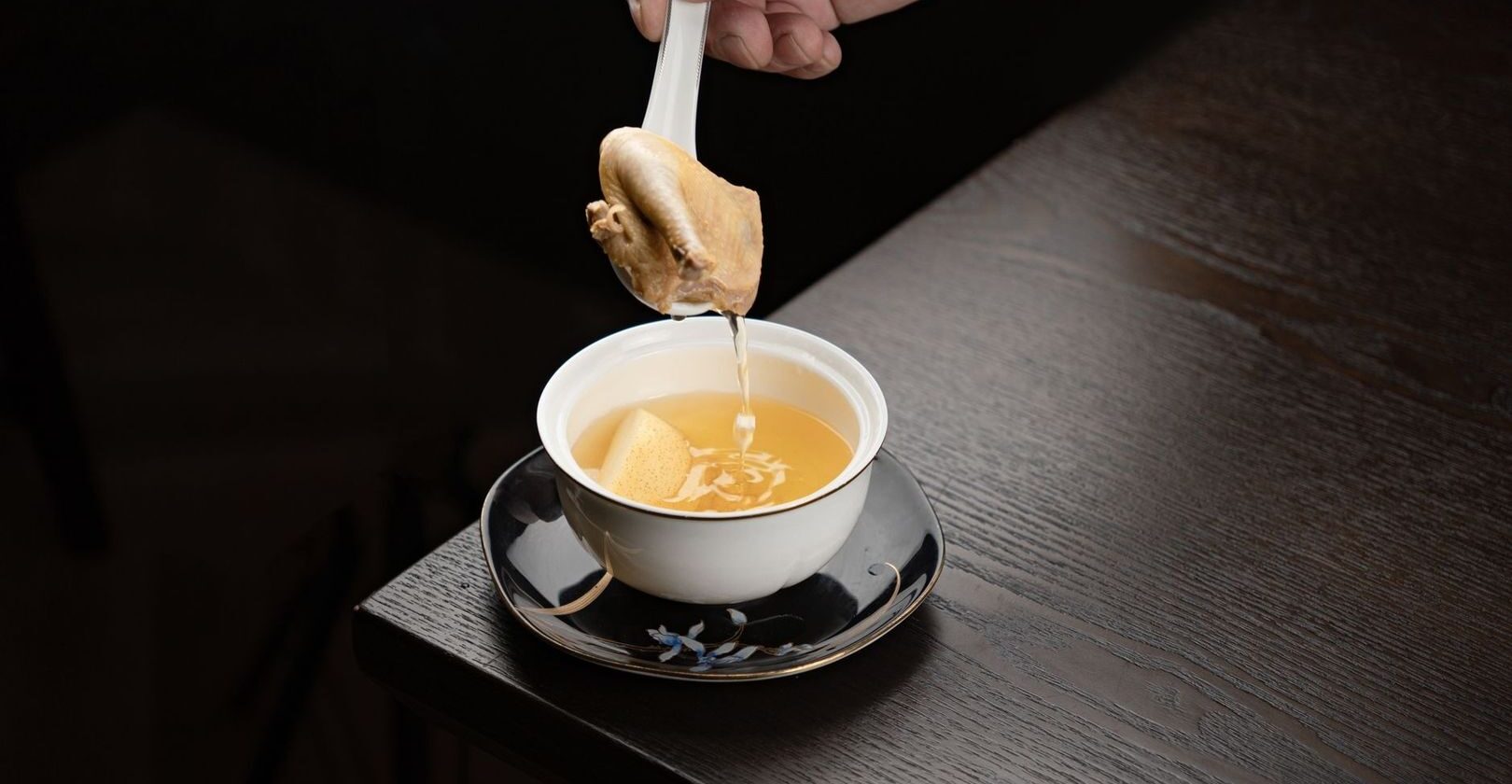 Une cuillère verse un bouillon doré dans une tasse blanche