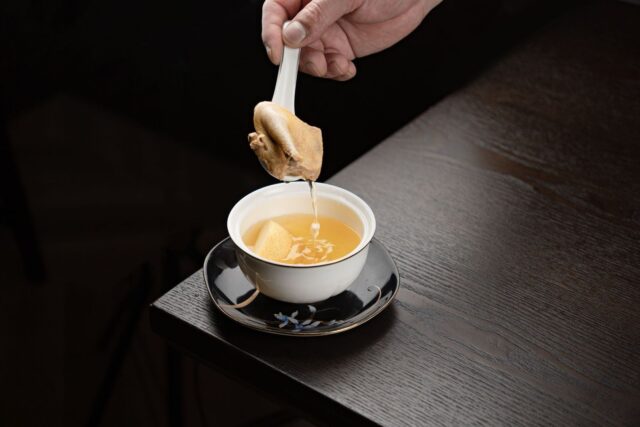 Une cuillère verse un bouillon doré dans une tasse blanche
